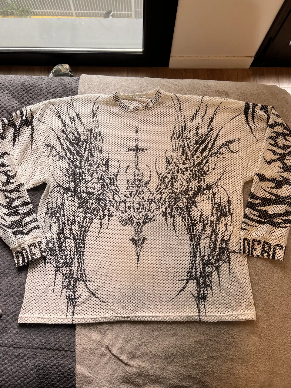 Remera de manga larga de red con estampado gráfico en negro. Diseño con detalles de alas y cruz en el frente, y estampado en las mangas. Ideal para un look streetwear o rave.
Equivale a un L/XL