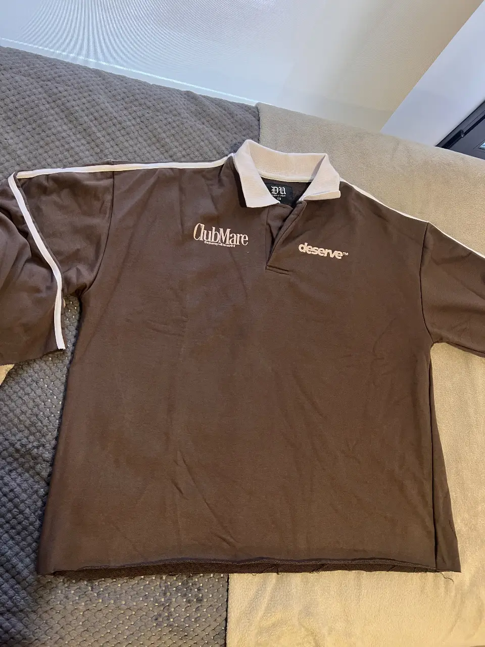 Buzo/ remera manga larga marrón con detalles blancos. Cuello polo con logo 'ClubMare' y 'deserve' estampado. Estilo deportivo y casual. Tela algodón rústico 