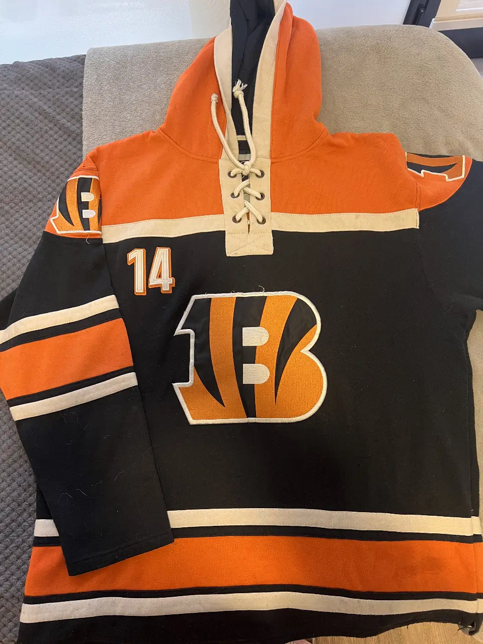 Buzo canguro de los Bengals de la NFL. Con capucha y cordones, el diseño incluye el número 14 y el logo "B" del equipo. Tiene detalles, por ejemplo una mancha que se aprecia en la foto de la espalda, la tapa la capucha.