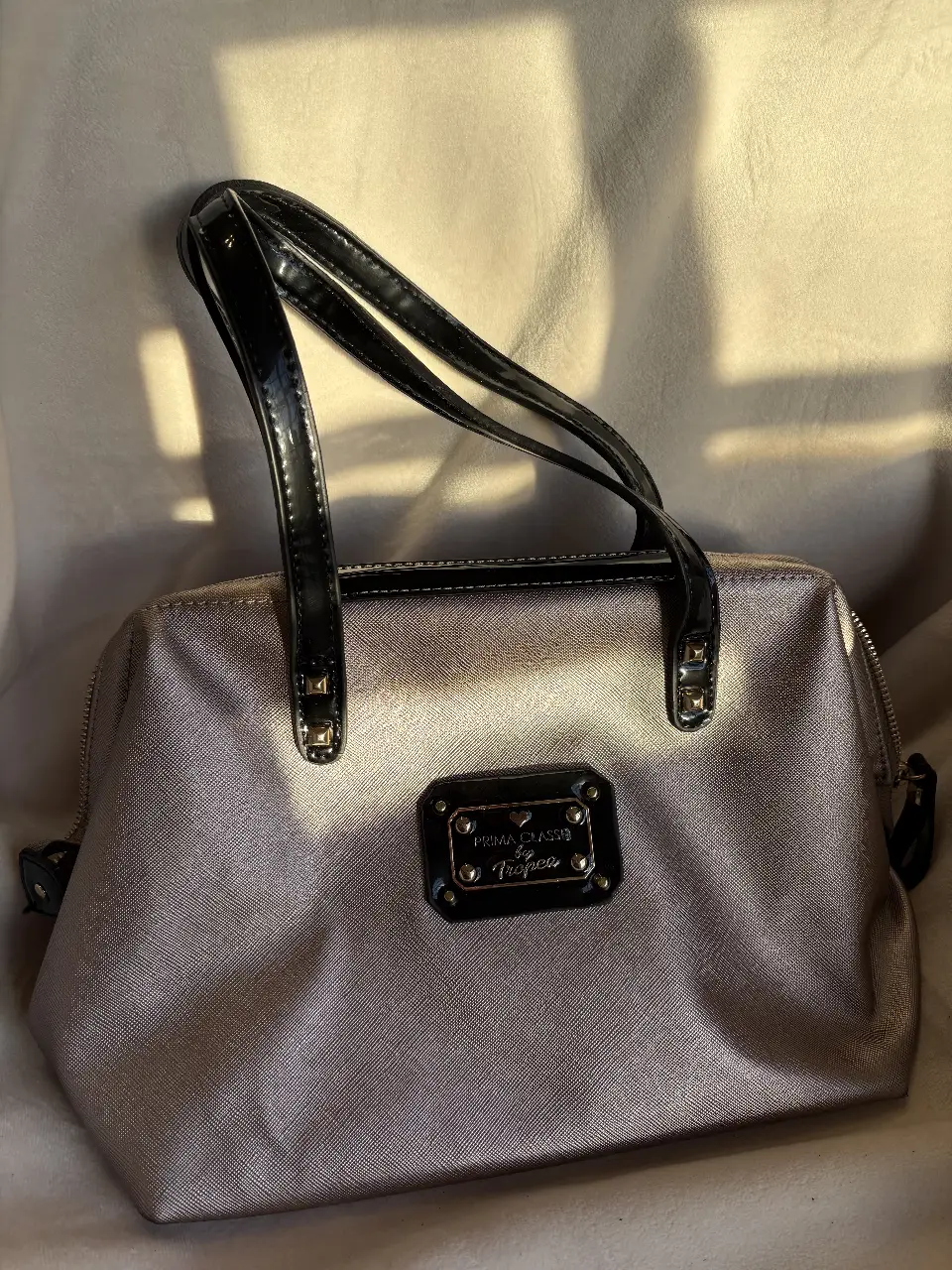 Cartera de mano Prima Classe by Tropea, color gris con detalles en negro. Ideal para llevar tus esenciales con estilo.