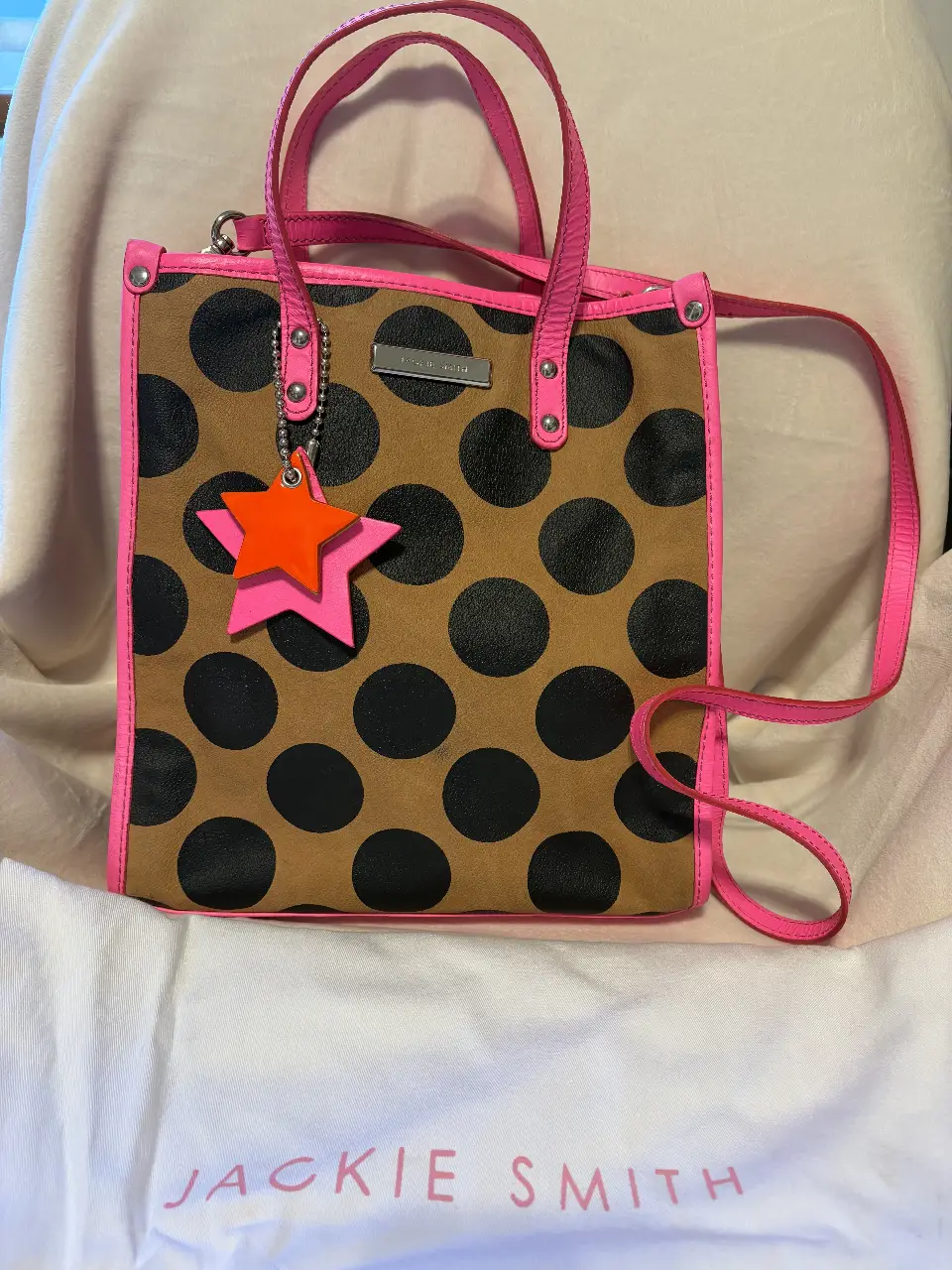 Cartera Jackie Smith con diseño de lunares negros sobre fondo marrón, detalles en rosa y dije de estrella. Ideal para un look moderno y llamativo.