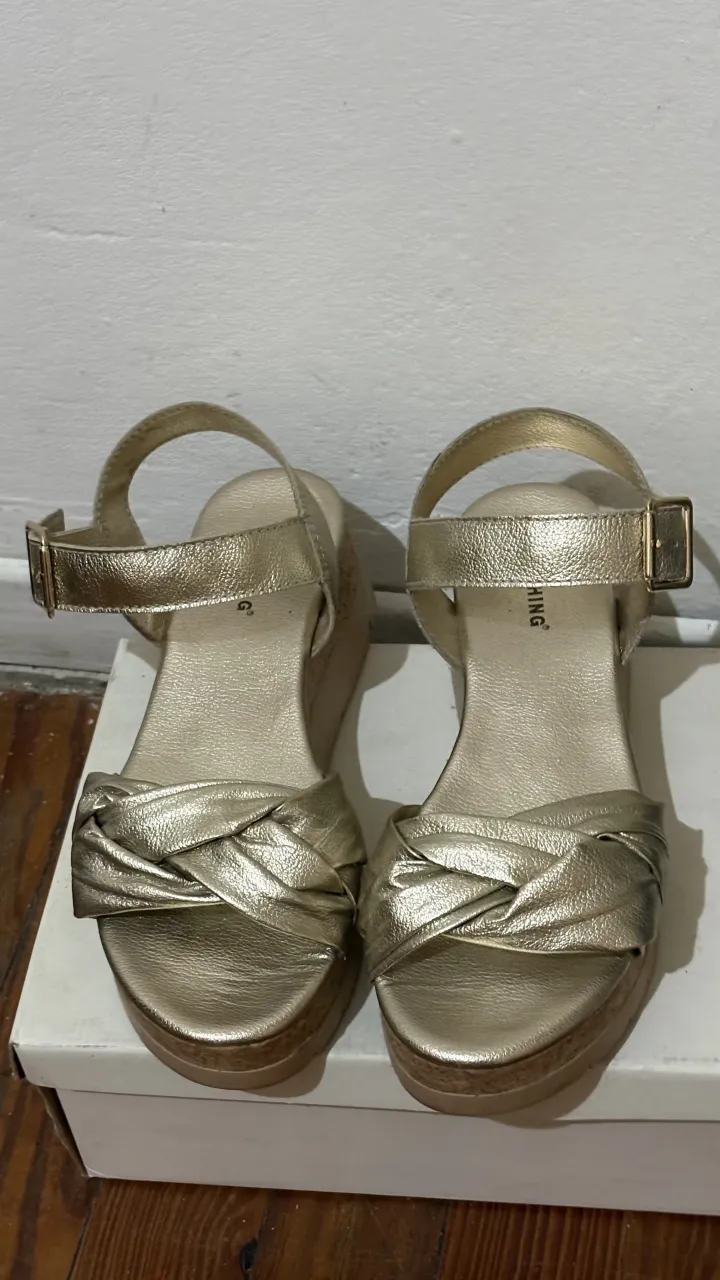Sandalias doradas con tiras cruzadas en la parte delantera y hebilla ajustable en el tobillo. Plataforma y taco cuña.