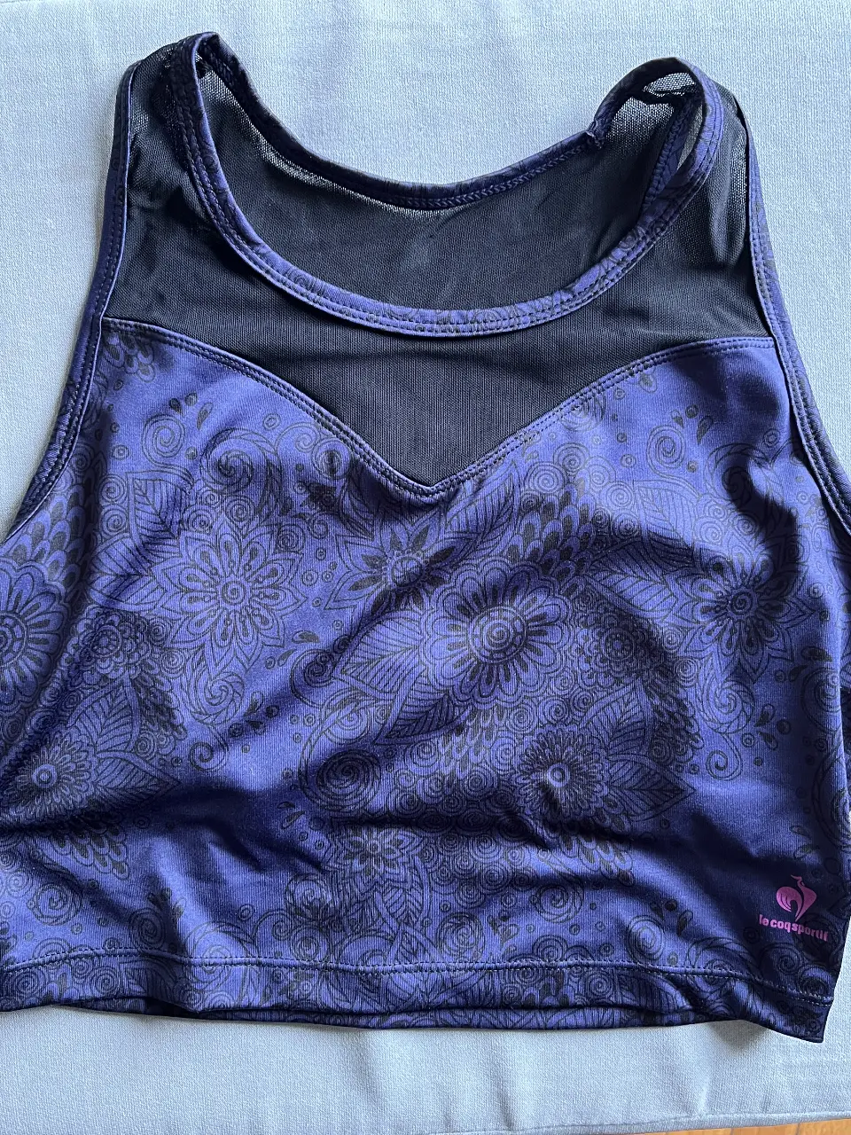 Top deportivo Le Coq Sportif para mujer, con estampado floral en tonos violetas azulados  y detalles en negro. Ideal para actividades de fitness y entrenamiento. Cuenta con un sujetador interno. Talle 42/44.