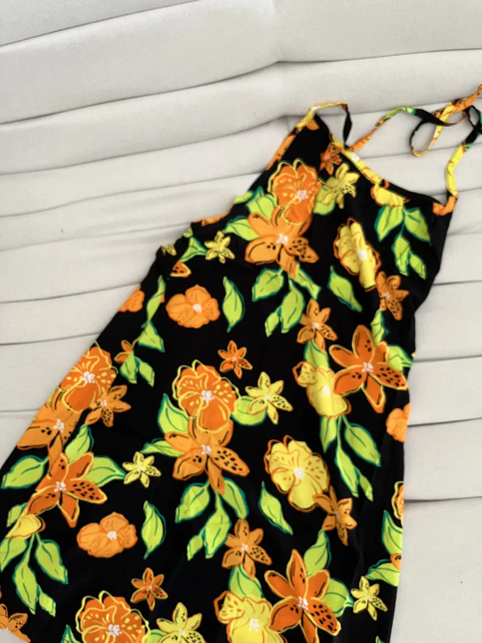 Vestido mini con estampado floral en tonos naranja, amarillo y verde  sobre fondo negro. Diseño con tirantes finos y espalda descubierta, ideal para el alto verano. Marca: Potra indumentaria 