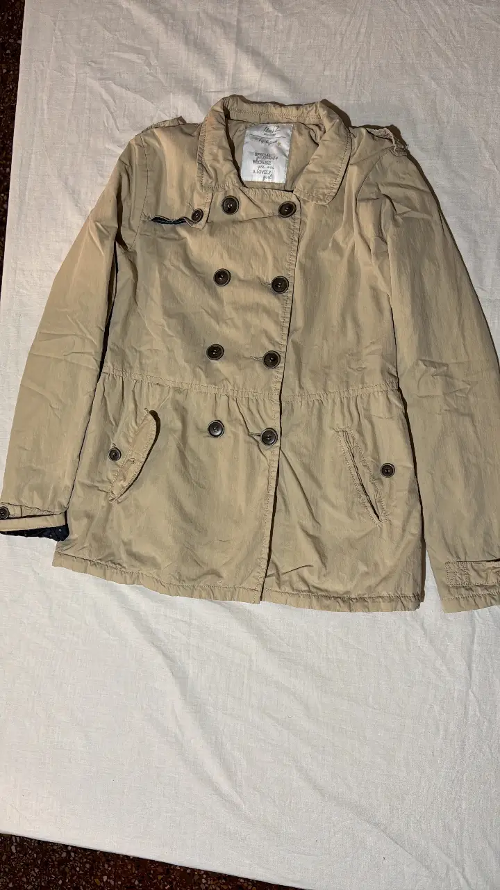 Campera estilo trench en color crudo, con botones y bolsillos. Ideal para un look casual y versátil.