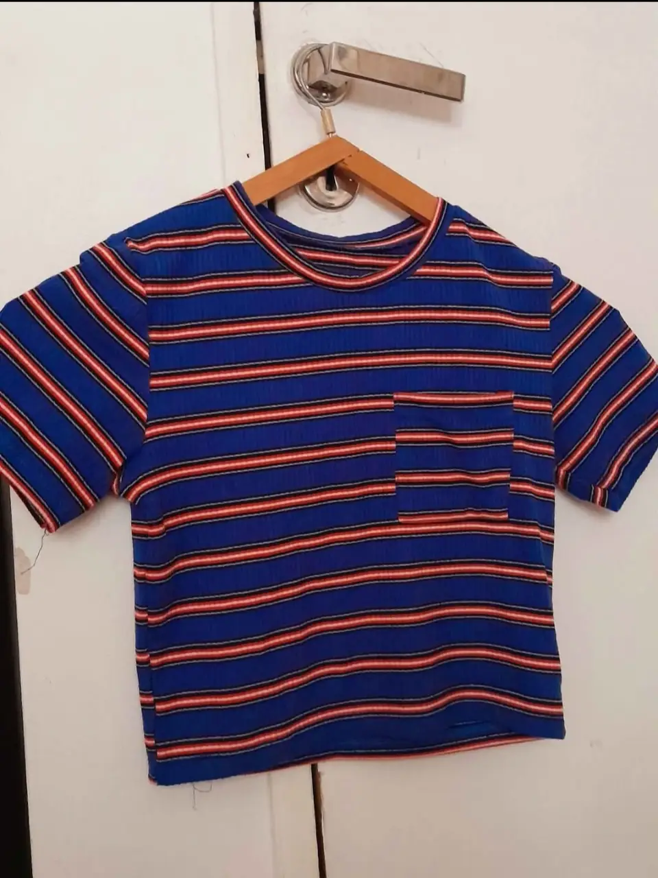 Remera de manga corta a rayas horizontales en azul con detalles en rojo y blanco. Tiene un bolsillo en el pecho. Ideal para un look casual y cómodo.
