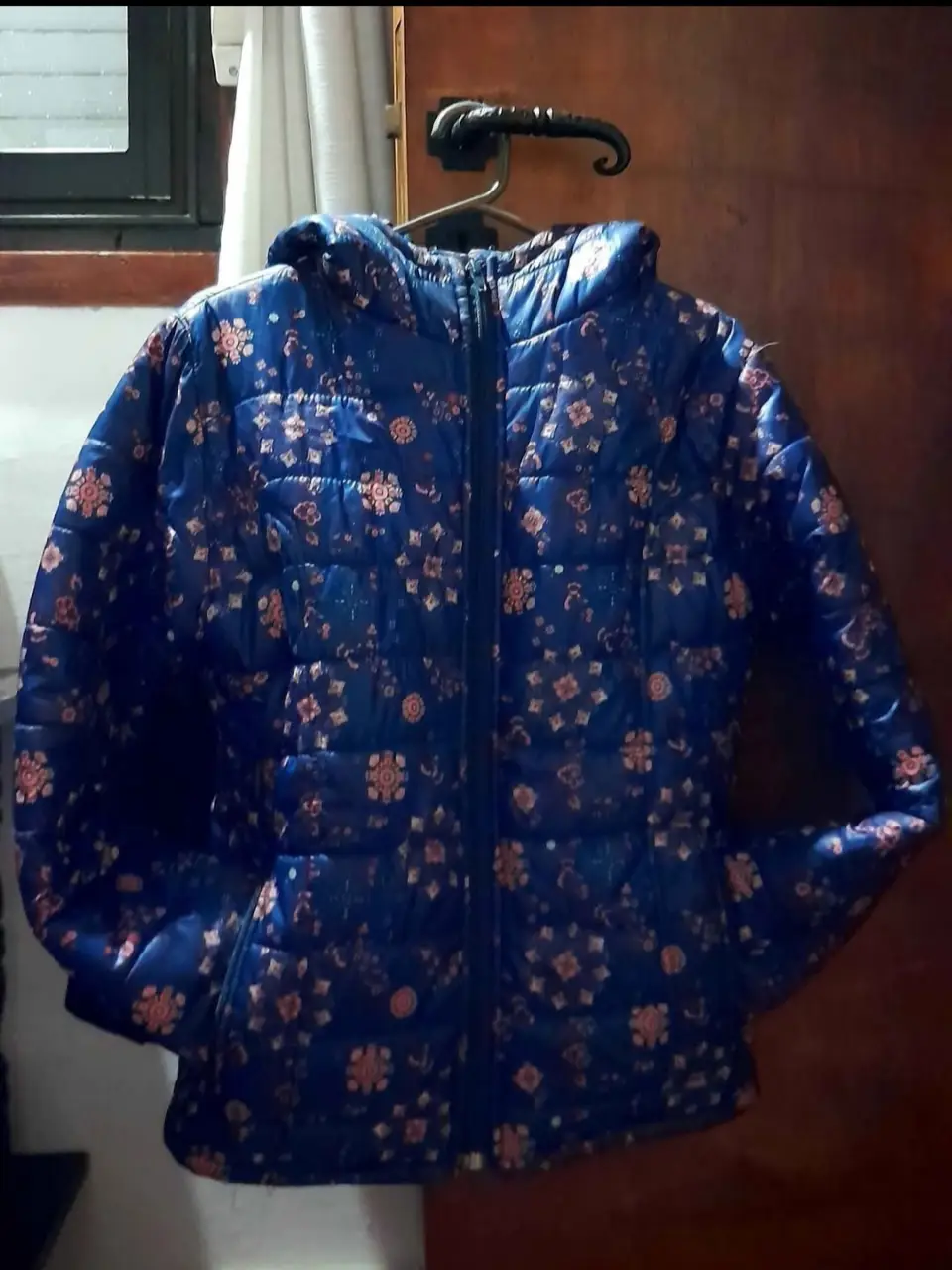 Campera de pluma azul con estampado floral en tonos rosados. Ideal para el invierno, con capucha y cierre. Perfecta para un look casual y abrigado.