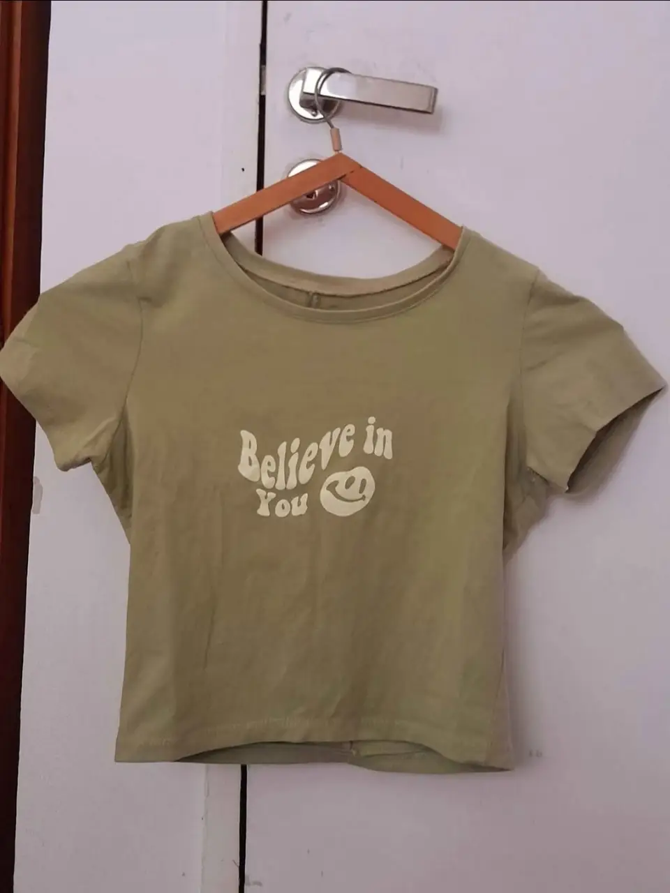Remera de manga corta verde con estampado "Believe in You" y un emoji sonriente. Ideal para un look casual y cómodo.