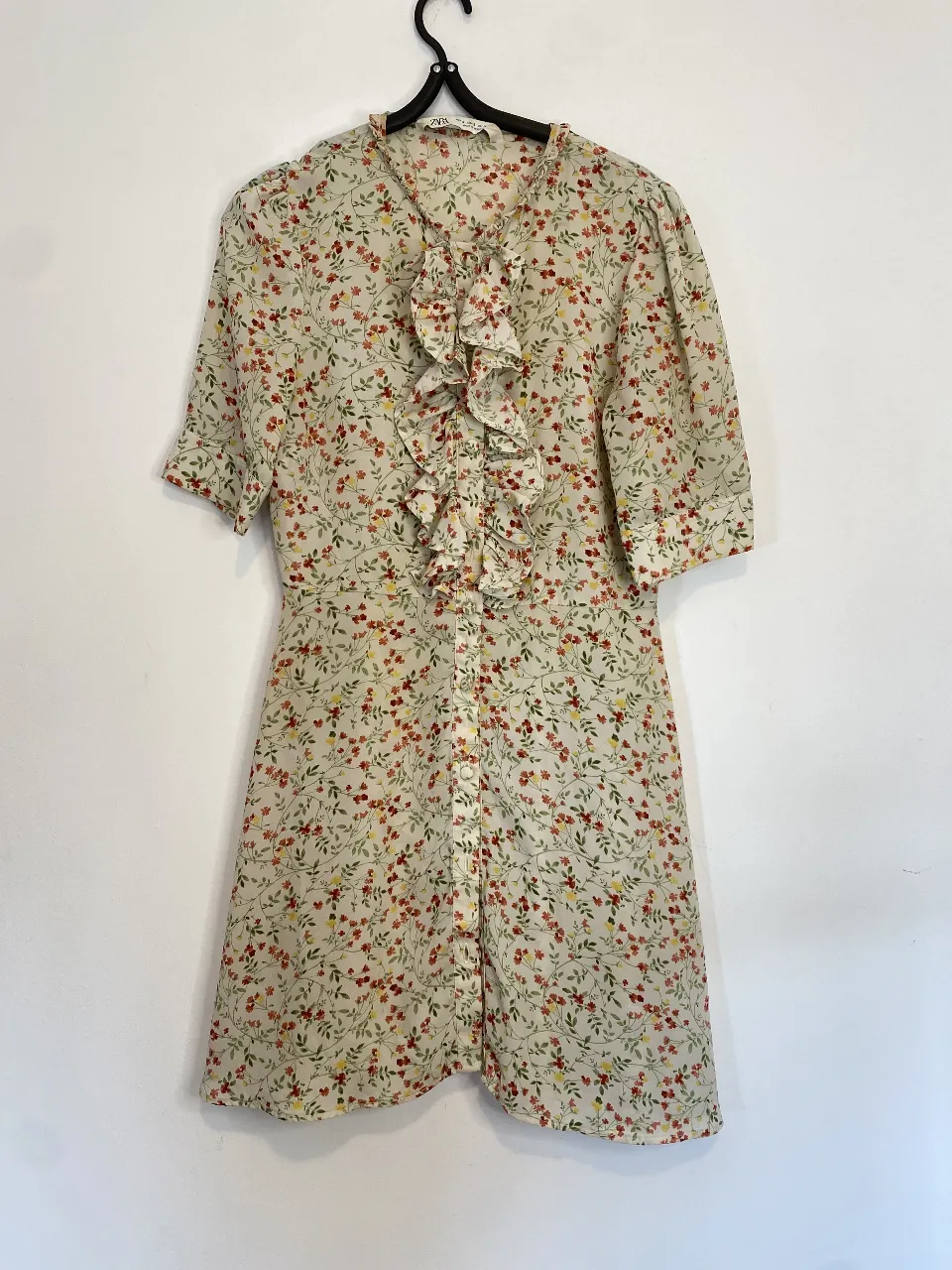 Vestido mini de mujer con estampado floral, detalle de volantes en el frente y mangas cortas. Ideal para un look fresco y femenino. Único detalle le falta el anteúltimo botón. Hombros 34 axilas 41 largo 83