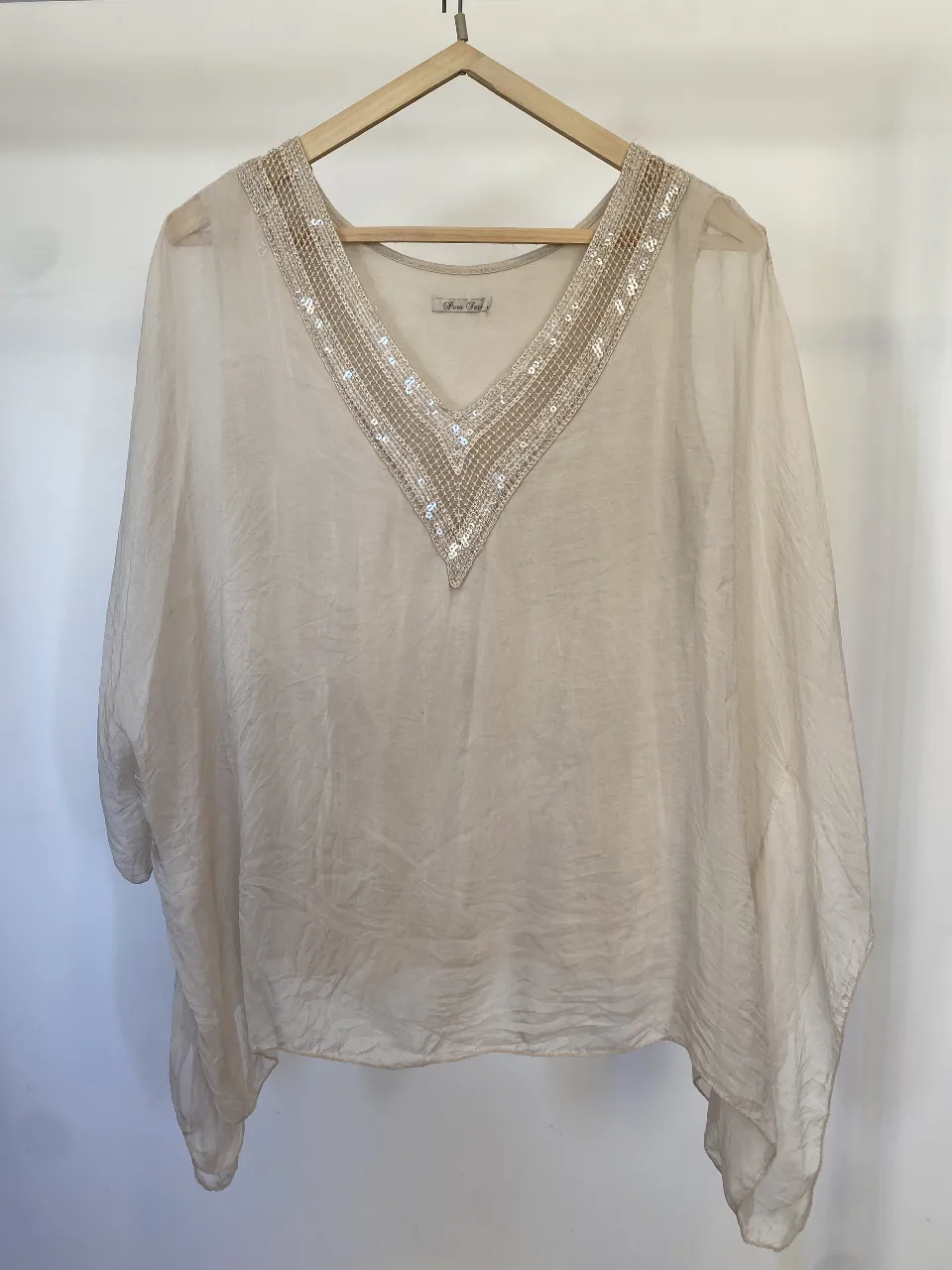 Blusón tipo capa de seda italiana color crudo con cuello en V adornado con lentejuelas. debajo tiene una remera tipo forro. Ideal para un look elegante y sofisticado. Detalle esa manchita que se ve en la foto