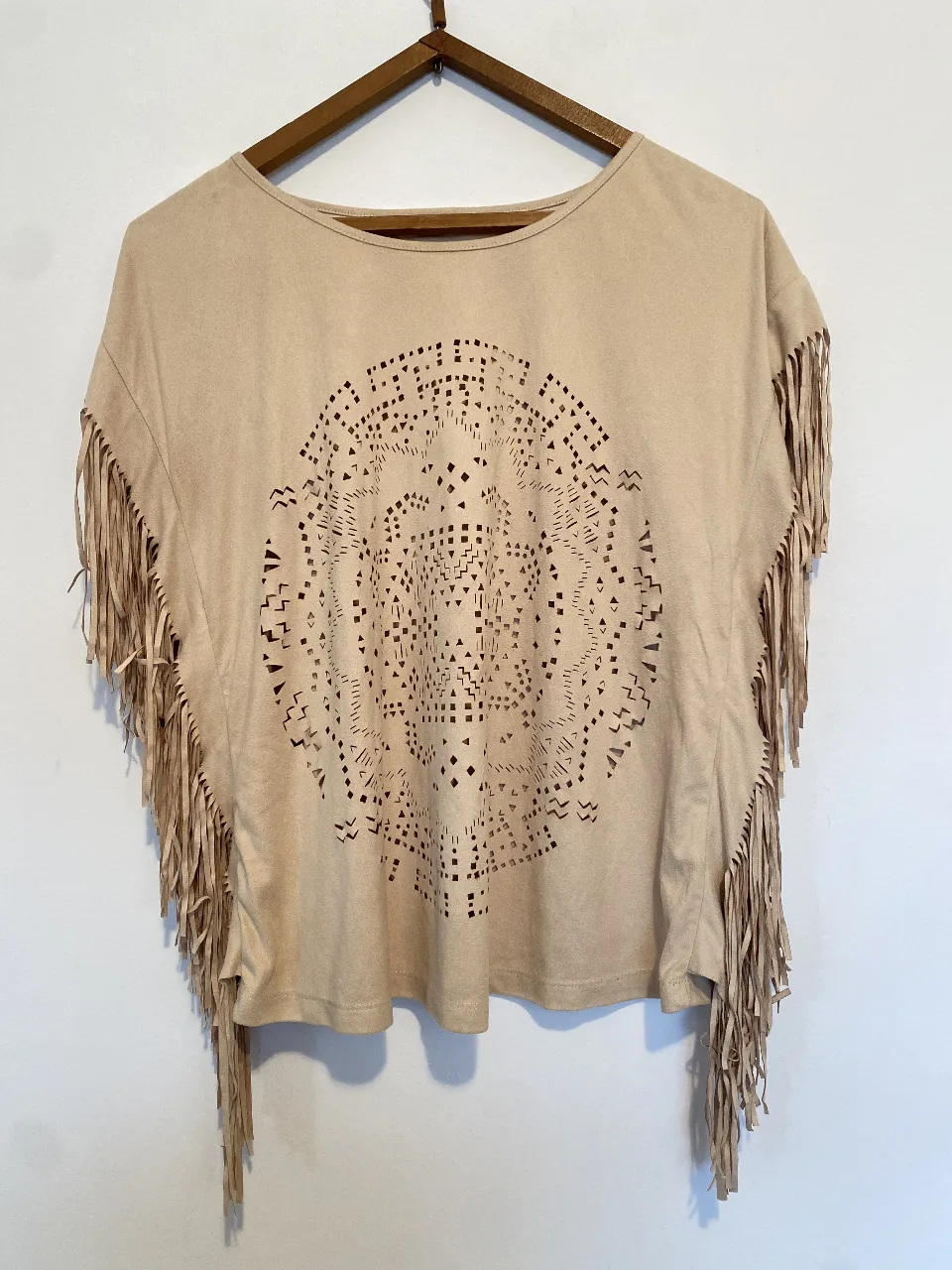 Blusa de gamuza sintética color crudo con flecos en las mangas y un diseño calado en el frente. Ideal para un look boho chic. Axilas 50, largo 60