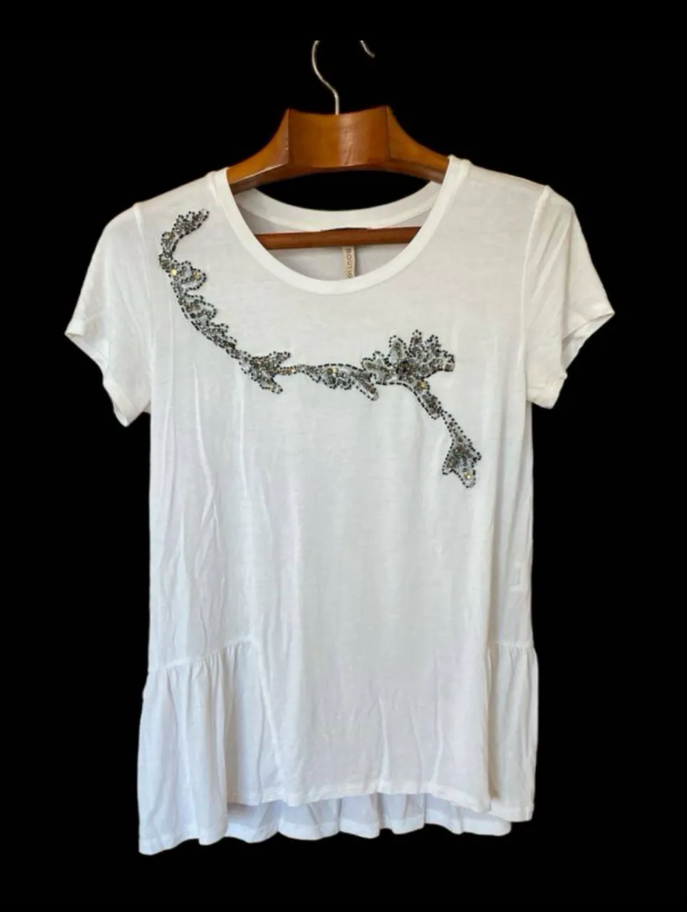Blusa blanca de mujer, con detalle de aplique bordado en la parte delantera. Diseño con volados en la parte inferior y mangas cortas. Ideal para un look casual y elegante.