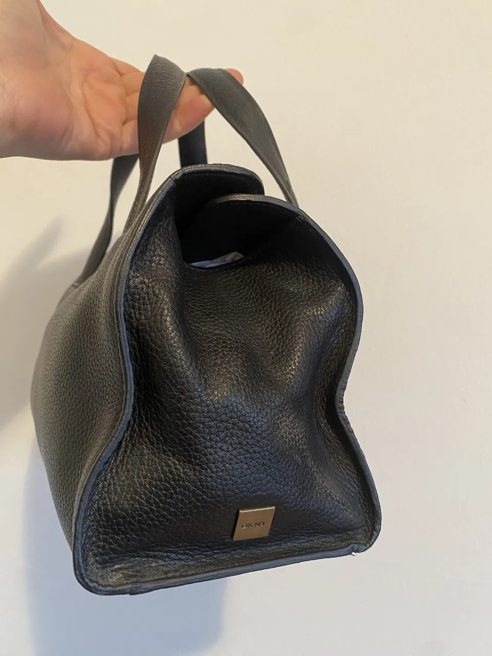 Cartera DKNY negra de cuero con manijas cortas, cierre imantado y detalle de logo dorado. Ideal para llevar tus esenciales con estilo y elegancia. por la base mide 10x24 cm corra 33cm y x el frente 15cm de alto x 24cm de ancho