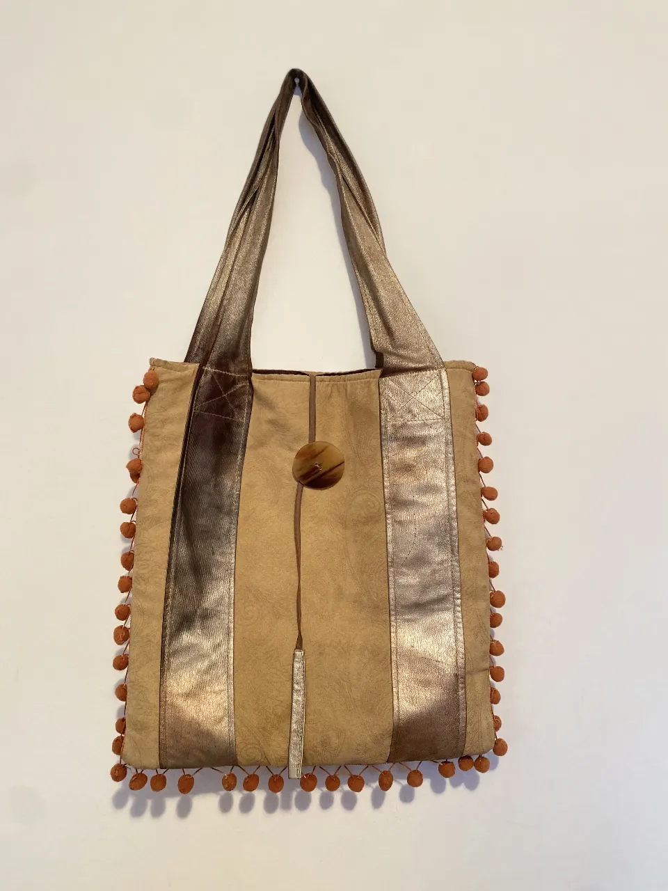 Bolso tote de mujer, estilo boho, con detalles artesanales. Confeccionado en materiales sintéticos, presenta un diseño con apliques dorados y pompones decorativos. Ideal para un look casual y con estilo. 35 × 38, Correa 65