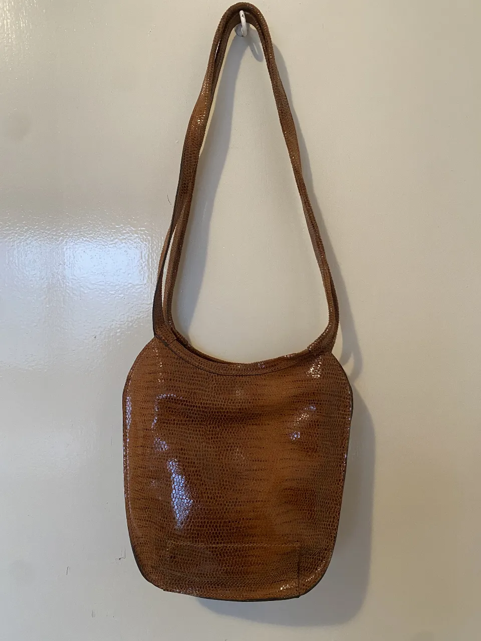 Cartera de hombro marrón de cuero  con textura de reptil. Diseño elegante y versátil, ideal para cualquier ocasión. Cuenta con un bolsillo con cierre en la parte trasera y un compartimento interno con cierre y etiqueta de la marca. Perfecta para un look sofisticado. 21x22 En la parte más ancha,  Correa 67. Importada de Italia
