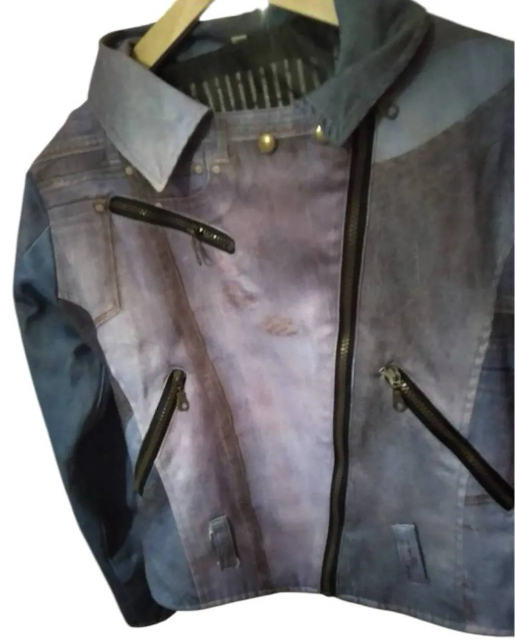 Campera biker de jean con estampado de diseño único. Posee cierre asimétrico y detalles de cremalleras. El diseño trasero presenta un estampado llamativo. El único detalle tiene un bolsillo un poco descosido