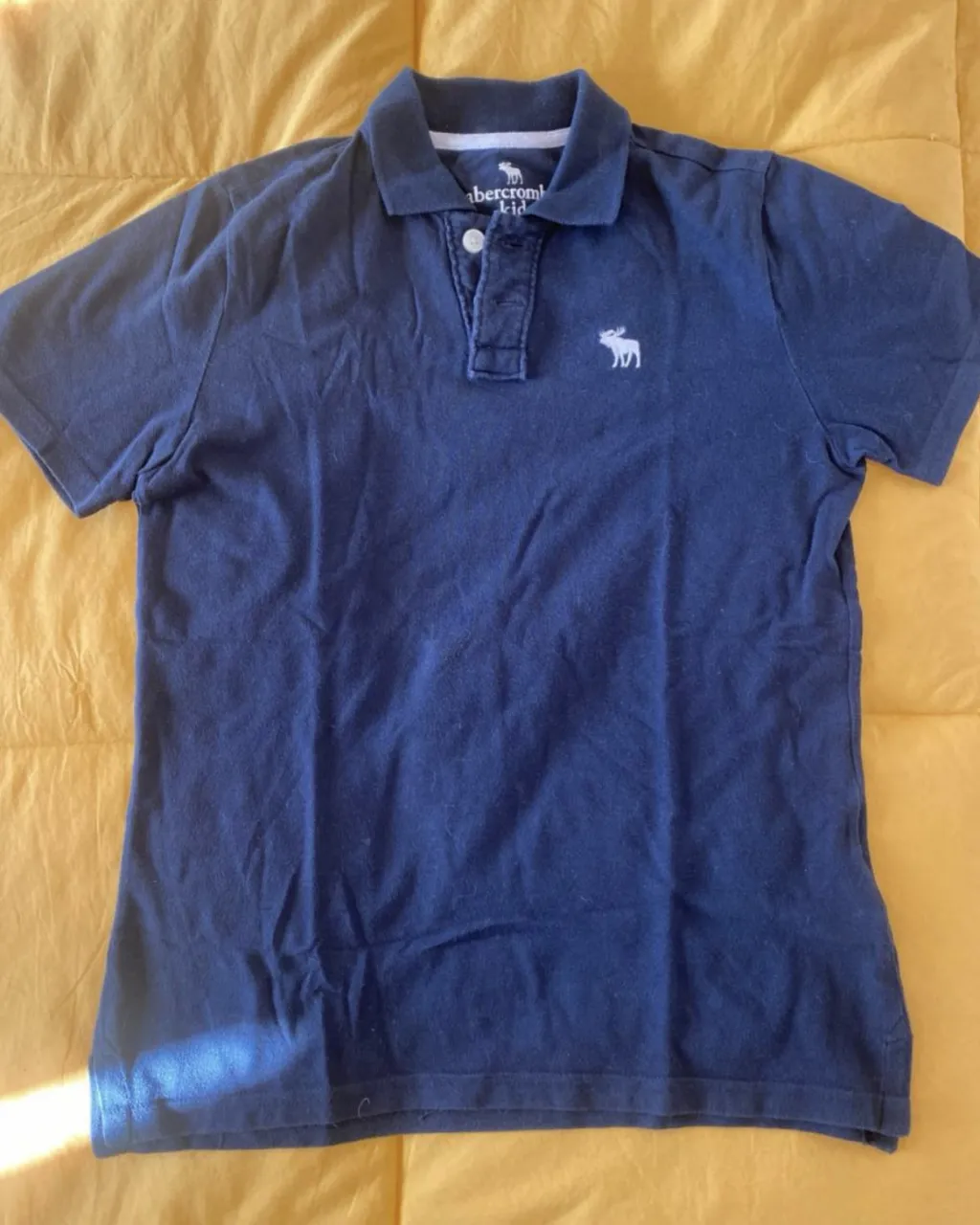 Remera polo azul marino de la marca Abercrombie Kids, con el logo del alce bordado en blanco. Ideal para un look casual y cómodo.