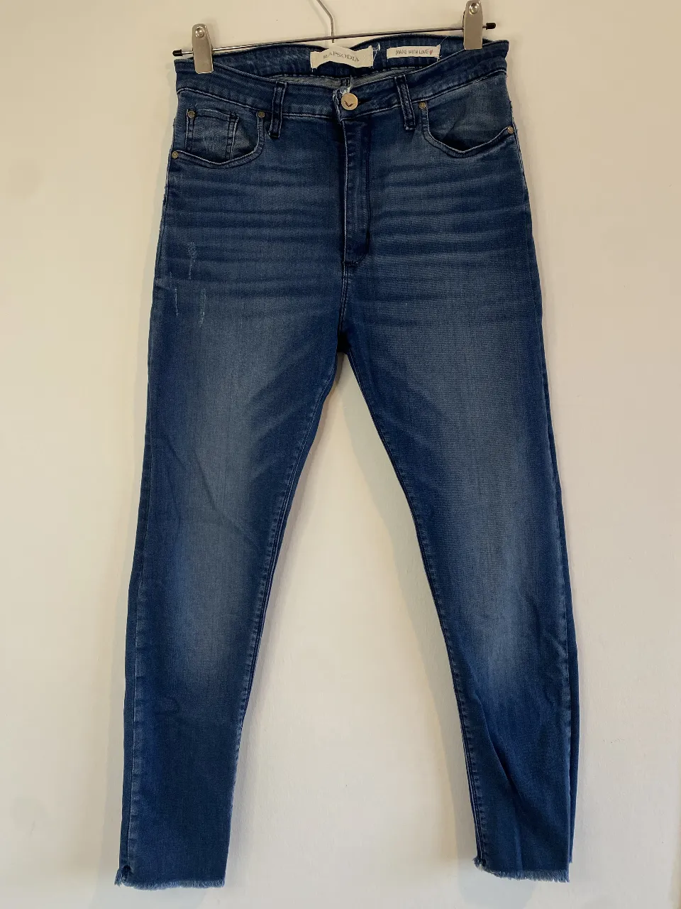 Jean Slim de mujer, tiro alto, color azul. Con detalles de desgaste y corte desflecado en el bajo. Marca Rapsodia. Único detalle, se ven en la foto en la parte del ojal