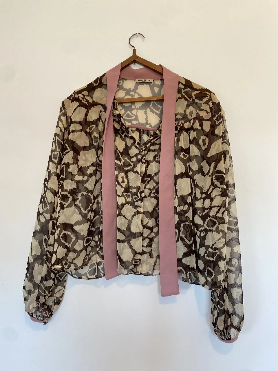 Blusa de mujer con estampado abstracto en tonos marrones y beige. Diseño con cuello y cinta rosa para atar. Ideal para un look elegante y sofisticado. Axilas 65