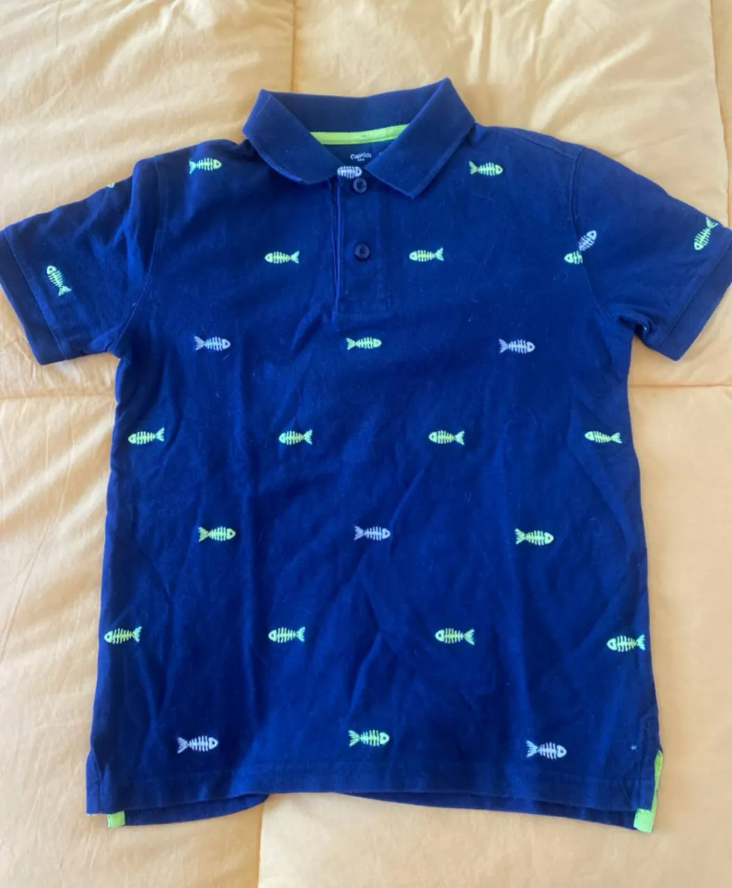 Remera polo azul marino para niño con estampado de peces en verde flúo. Cuello y detalles en verde. Ideal para un look casual y fresco.