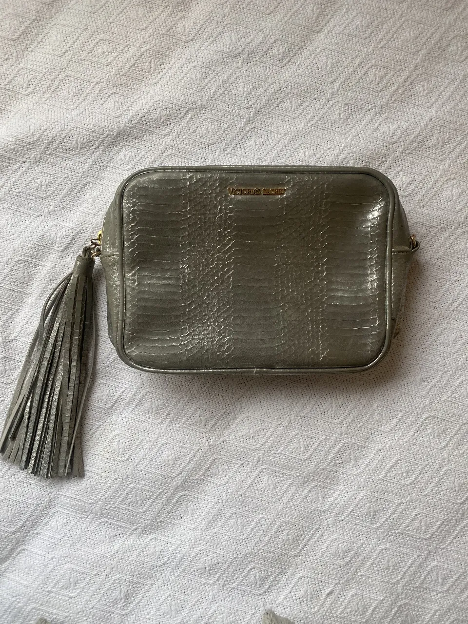 Cartera de mano de la marca Victoria's Secret, color plateado con textura de reptil. Posee un detalle de borla y el logo de la marca en dorado. Ideal para una salida. le falta la Cadena (era dorada) y detalles del cuero un poco  gastado en algunas partes 