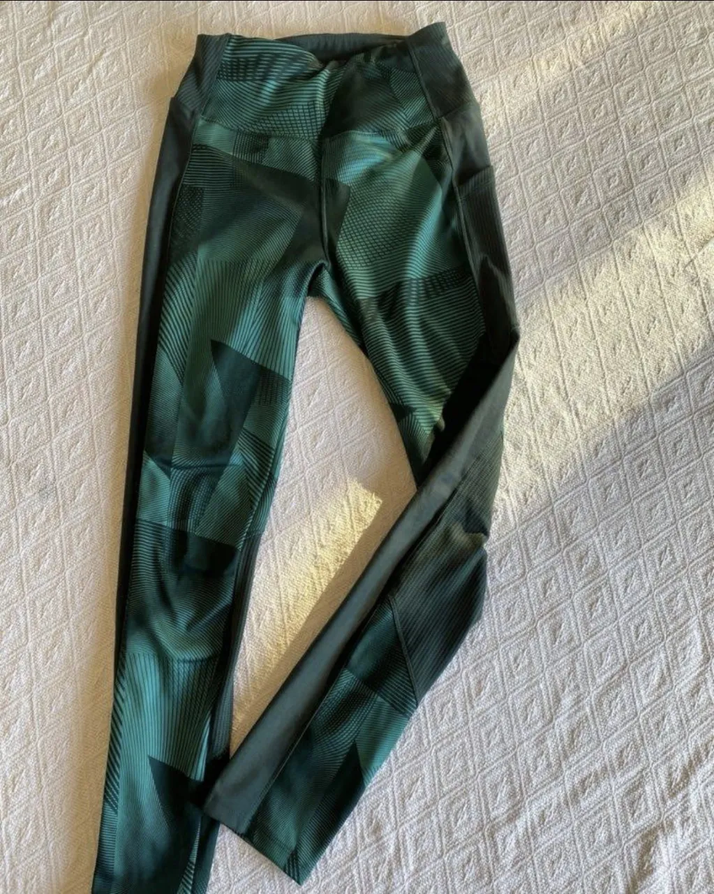 Calzas deportivas de mujer, color verde con detalles geométricos y paneles laterales en negro. Marca Domyos, ideales para actividades físicas.