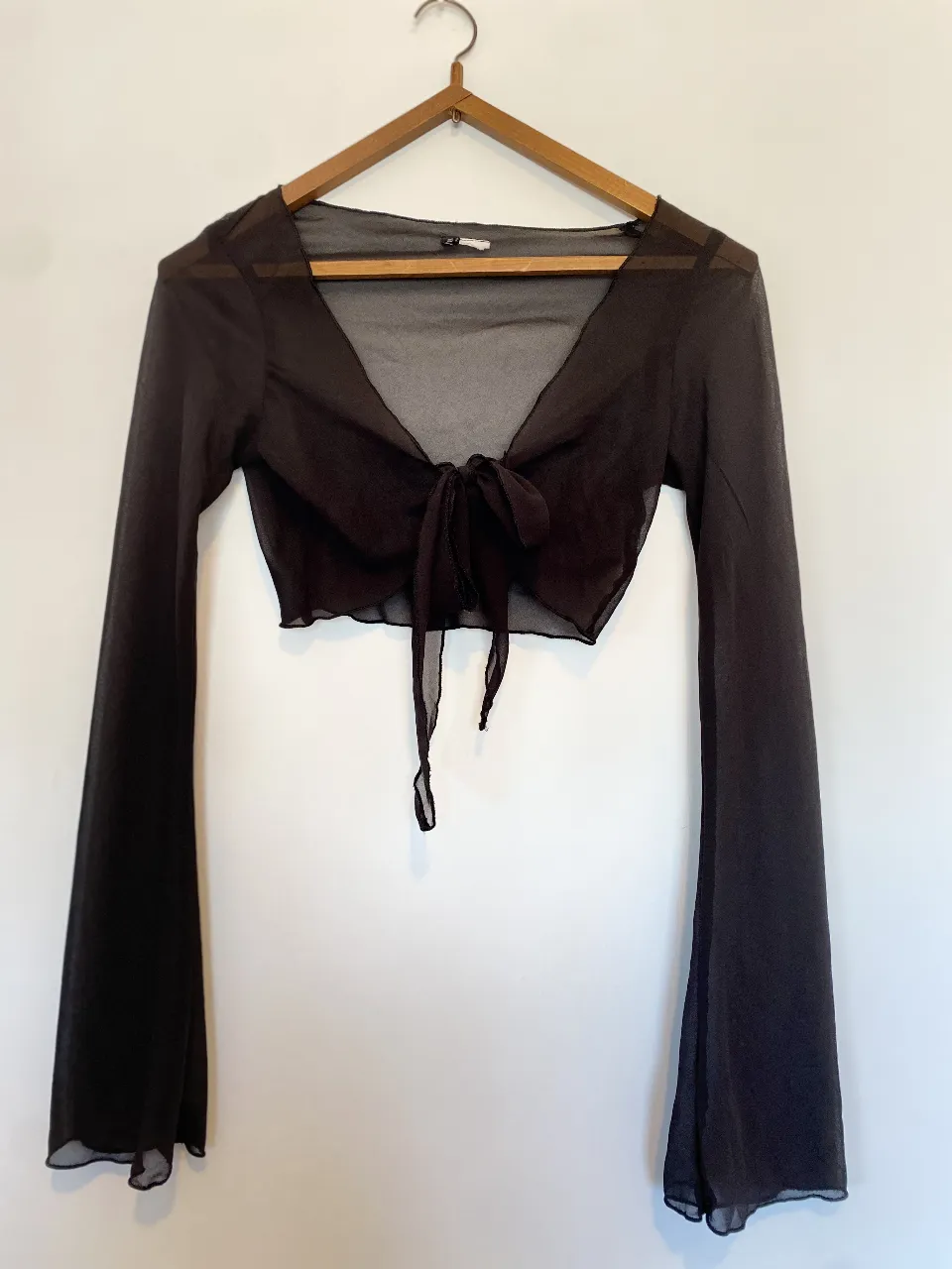 Top negro de manga larga con mangas acampanadas y detalle de lazo en el frente. Ideal para un look de fiesta o salida.