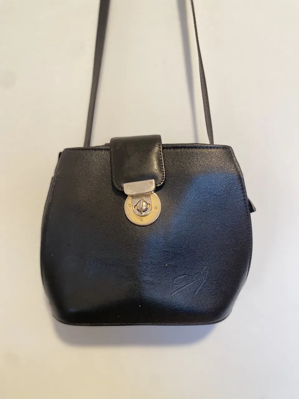 Cartera bandolera negra de cuero, con cierre y solapa con broche dorado. Ideal para llevar tus esenciales con estilo y elegancia. detalle: ese pequeño salido cerca de la lengüeta de cierre Y algún desgaste interior que se ve en la foto. parte más ancha 26cm, alto 20cm,  ancho de la base 8cm
