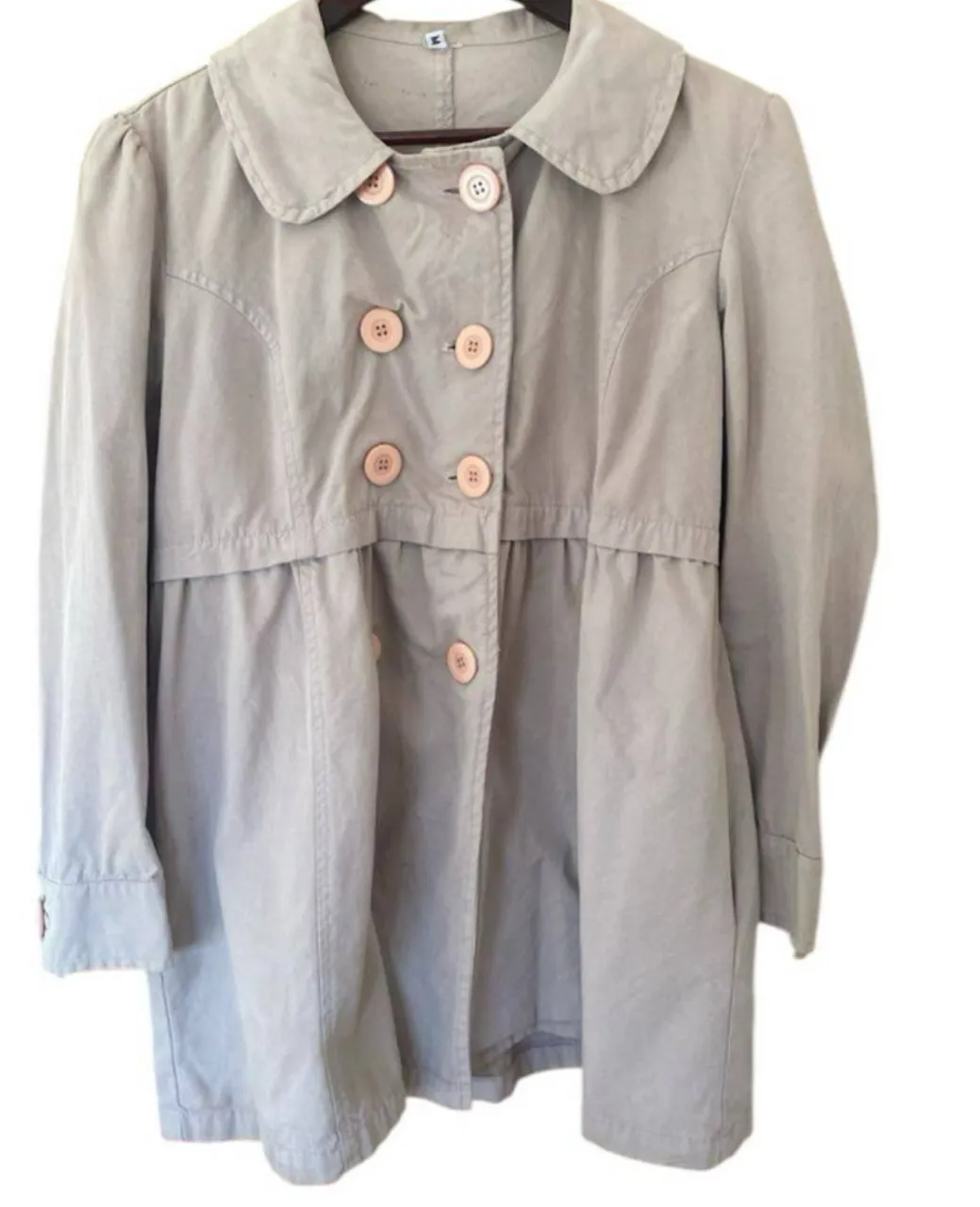 Trench  gris claro con botones rosados, estilo vintage, ideal para un look elegante y casual. Perfecto para la temporada de otoño. Único detalle esas manchitas del cuello