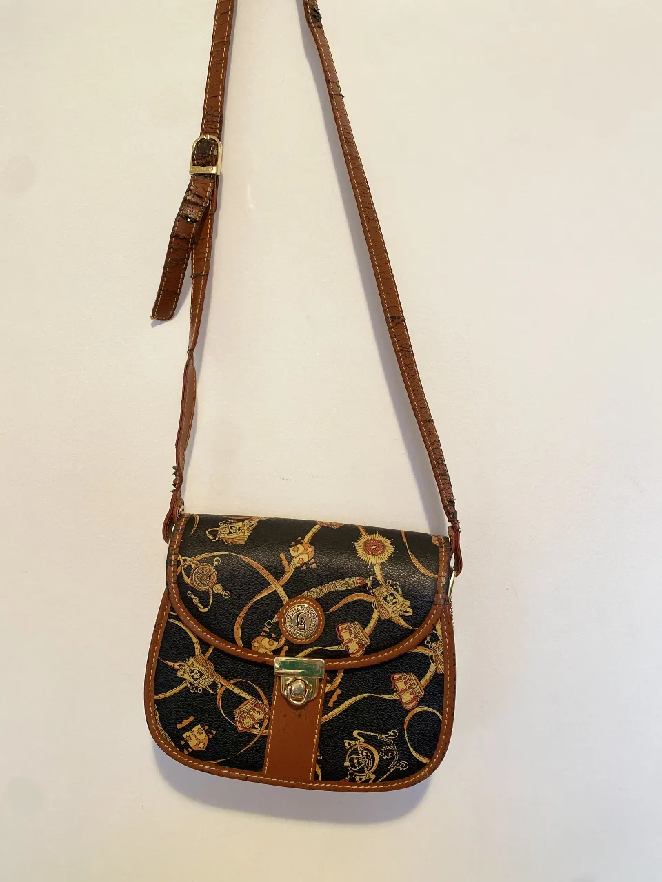 Bandolera vintage con estampado dorado y marrón. Diseño con solapa y cierre metálico. Detalles de cuero marrón en los bordes y correa ajustable. Ideal para un look retro y con estilo. material PU. Tiene los desgastes en las correas y tiras marrones. Por adentro tiene varios compartimientos. 
Los herrajes están perfectos 20 × 24 siete de profundidad