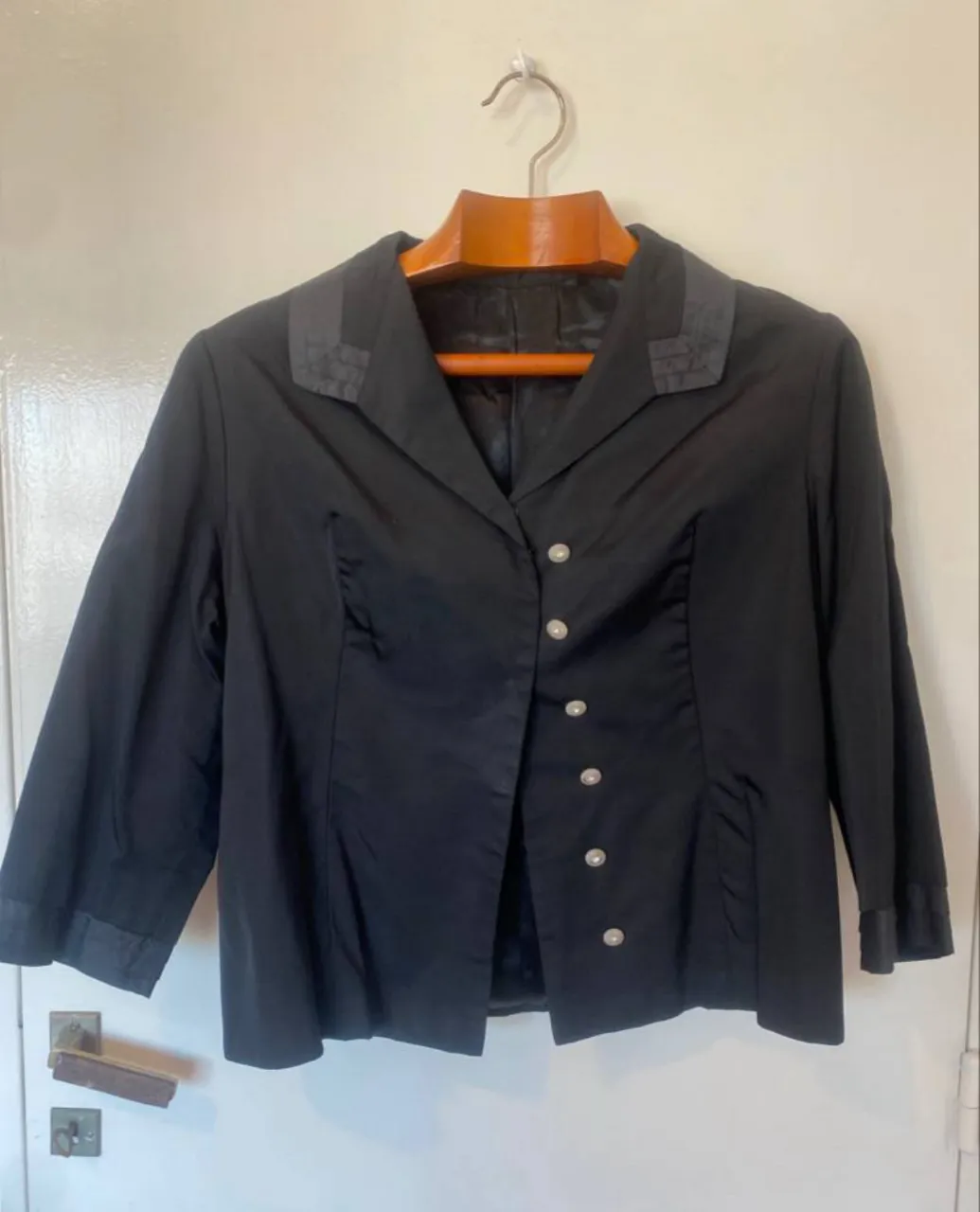Elegante blazer negro de mujer, con botones y detalles en el cuello. Ideal para un look formal o de trabajo.tiene tres botones clips originales y se le han cosido una hilera de botones blancos con unos ganchos para cerrar que se salieron 
tiene una pequeña costura en el borde de la solapa
está forrada y es una tela gruesita y semi brillante
hombros 41 
axilas 44 
mangas 43 
largo 54 