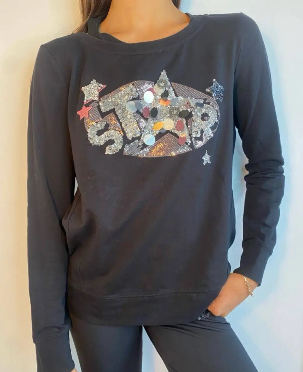Buzo de cuello redondo negro de mujer con aplique de lentejuelas con la palabra "STAR". Ideal para un look casual y canchero.