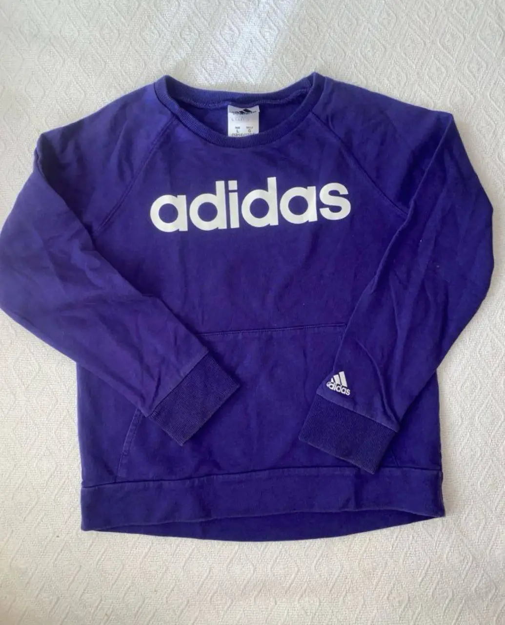 Buzo Adidas de cuello color violeta con el logo de la marca en blanco en el frente. Cuenta con bolsillo tipo canguro y puños en las mangas. mangas ranglan (desde el escote a al puño 56) ancho 41 largo delantero 47 largo trasero 49. puede ir para un s o xs