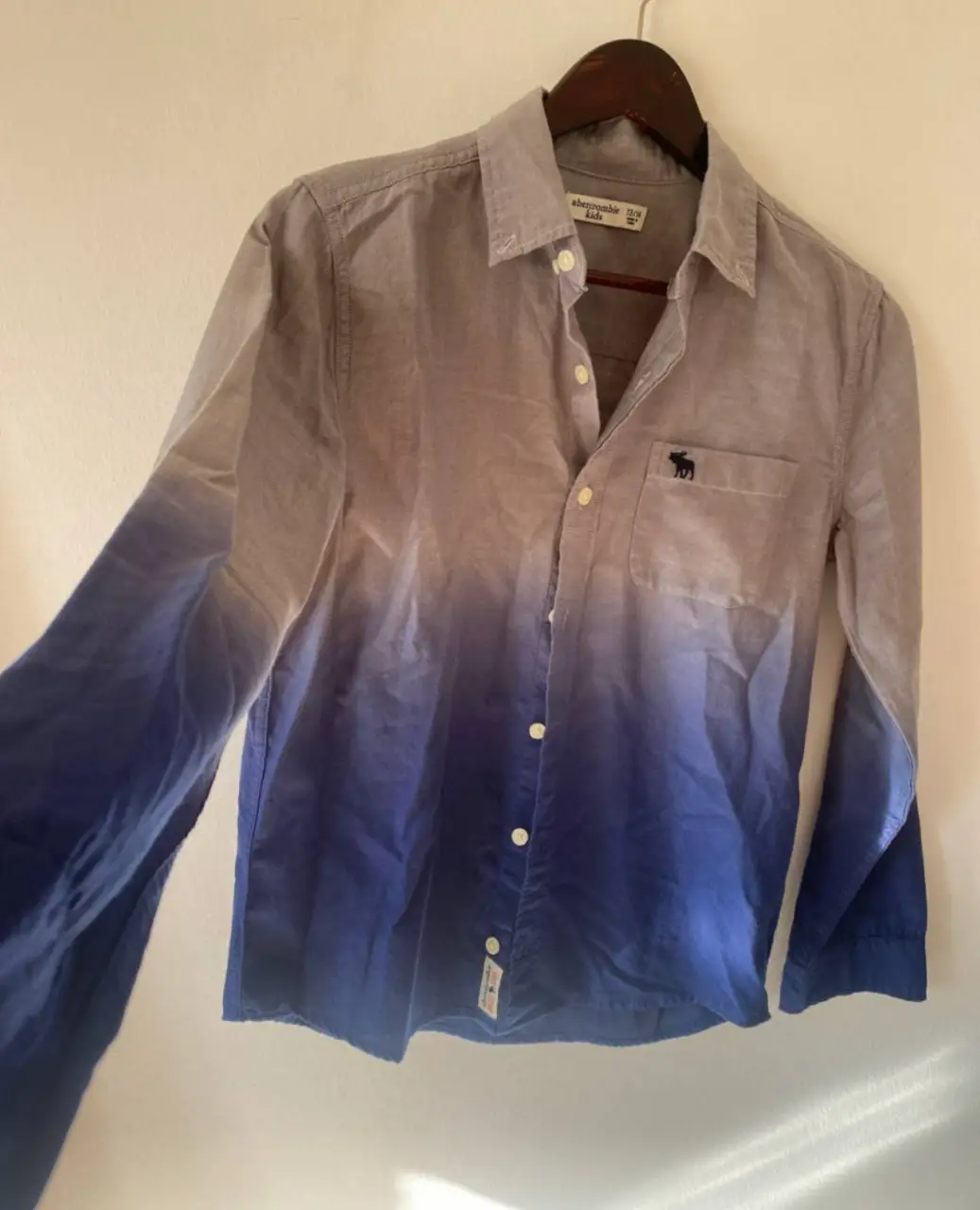 Camisa Abercrombie Kids para niño, con diseño degradado en tonos grises y azules. Manga larga, con bolsillo en el pecho y logo de la marca bordado. Ideal para un look casual y moderno.
