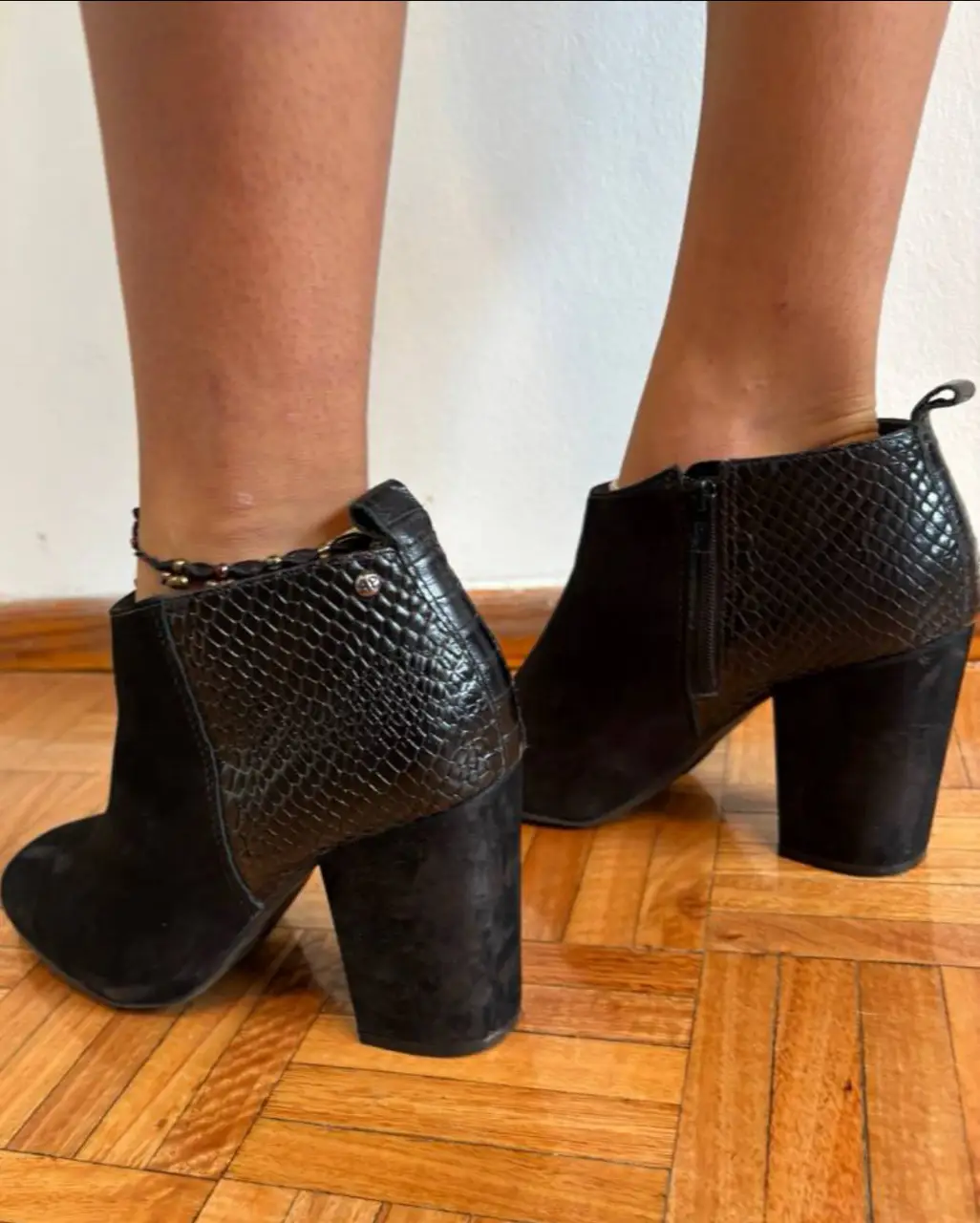 Botines negros de cuero con detalles de textura de reptil en el talón. Taco ancho y cierre lateral. Ideales para un look elegante y moderno.