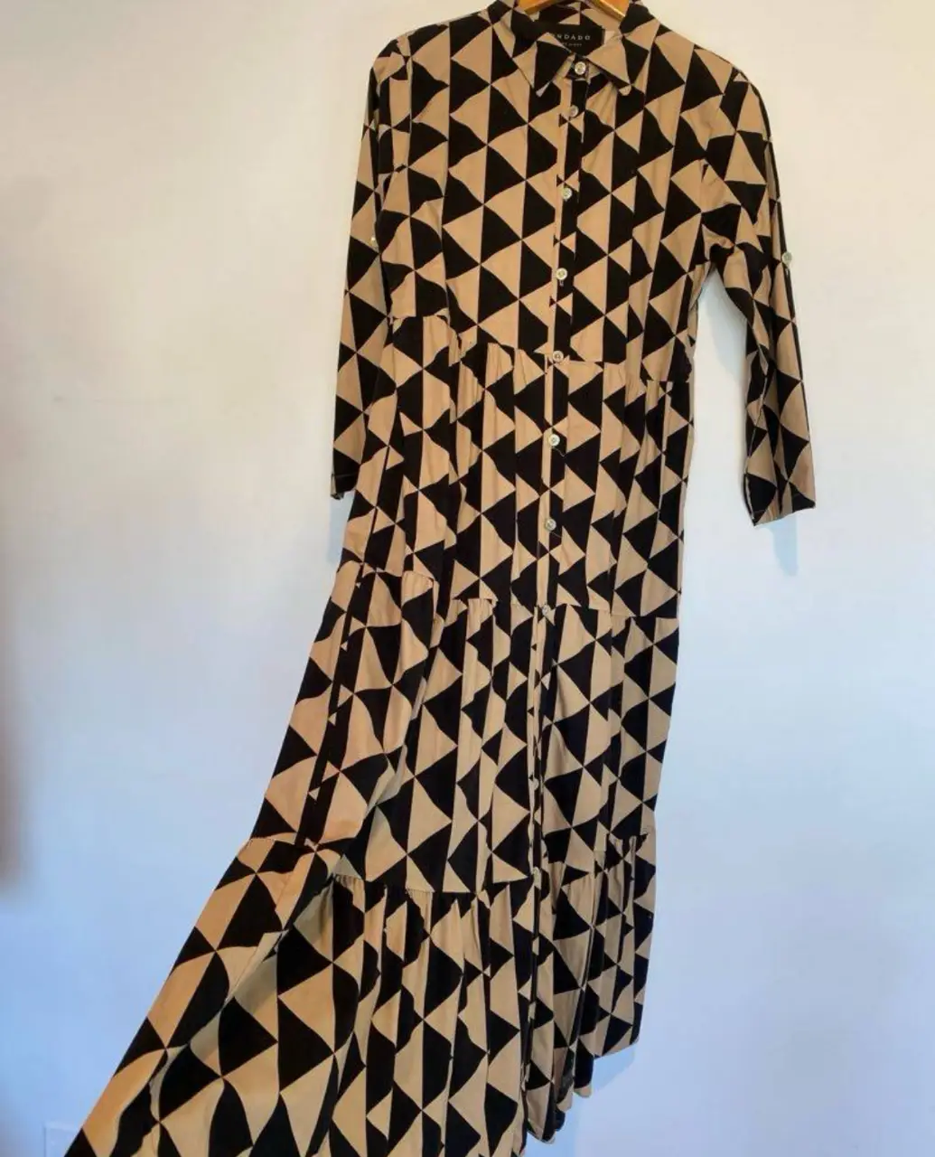 Espectacular vestido de diseño geométrico en tonos negro y crudo. Corte clásico con cuello camisero y cierre frontal con botones. Ideal para un look casual y moderno. no dice el talle pero ver medidas hombros 40, axilas 50, mangas 52 largo 129