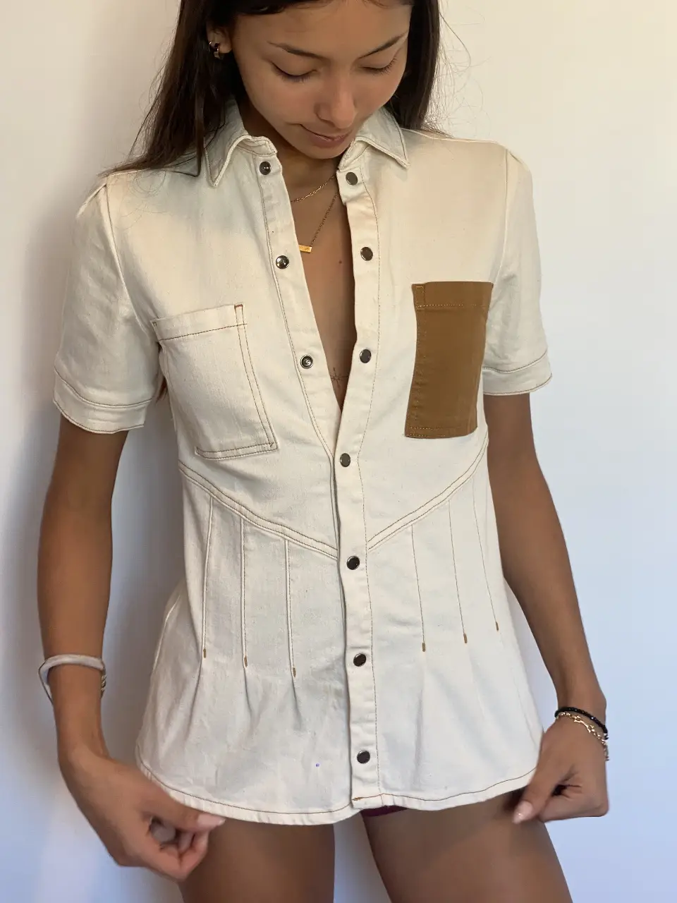 Camisa de mujer Jazmín Chebar de color blanco con un bolsillo marrón en el pecho. Tiene mangas cortas y botones. En la espalda tiene un parche con la inscripción "JET'AIME". 