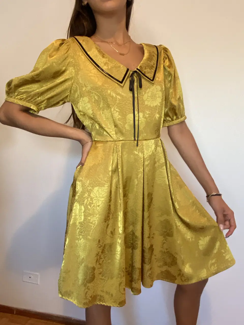 Vestido mini amarillo con cuello Peter Pan negro y lazo. Diseño vintage con mangas abullonadas y falda con vuelo. Ideal para un look elegante y retro. 