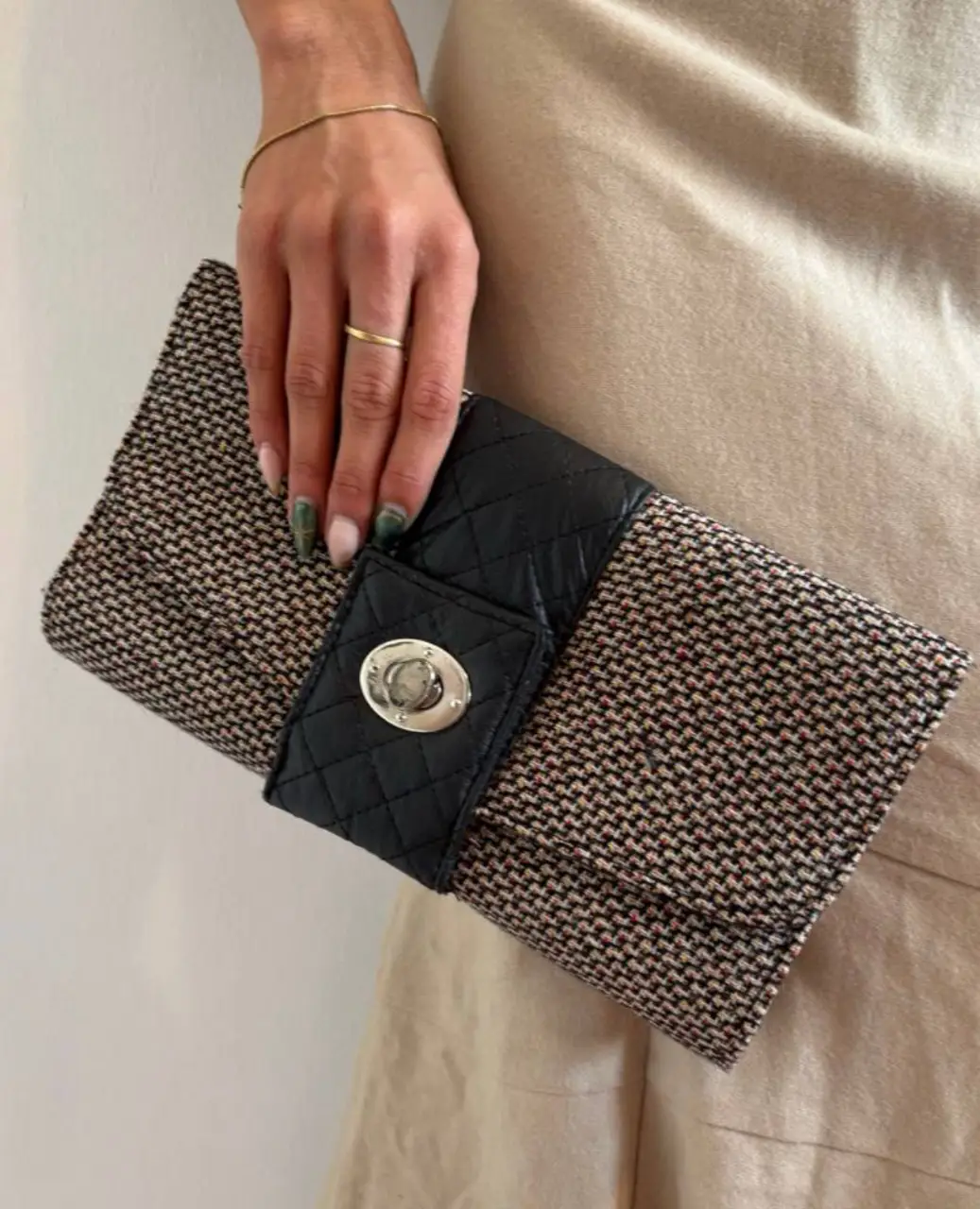Clutch de mano con diseño de tweed en tonos crudos y negros. Posee un detalle de cuero sintético negro acolchado en el frente con cierre metálico plateado. Ideal para eventos formales o salidas.