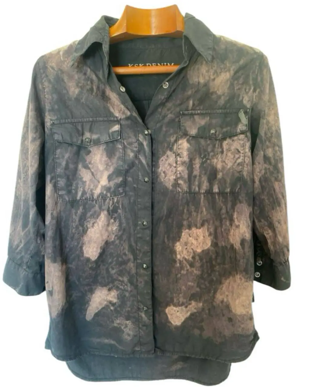 Camisa  KSK DENIM con estampado tie dye en tonos negros y marrones. Corte clásico con mangas 3/4, dos bolsillos delanteros y botones. Ideal para un look casual y moderno.