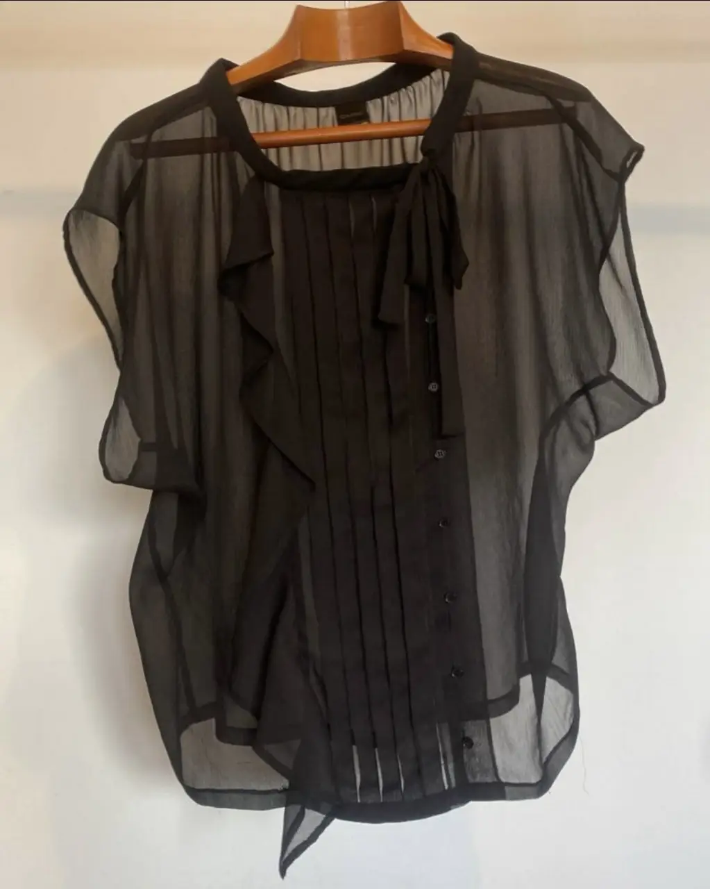 Blusa negra de gasa transparente con detalles de volados y lazo en el cuello. Ideal para un look elegante y sofisticado.