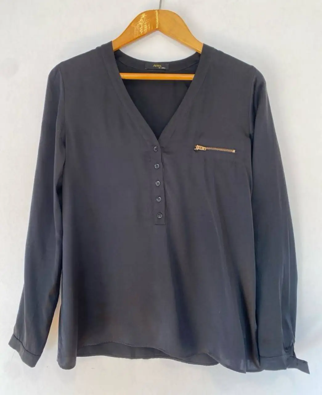 Blusa negra de manga larga con cuello en V y detalle de cierre dorado en el pecho. Ideal para un look elegante y versátil.
