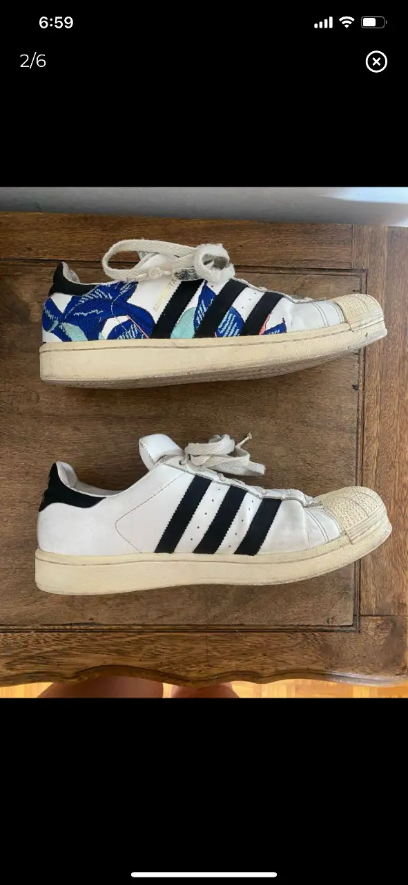 Zapatillas Adidas Superstar blancas con detalles en negro y diseños en azul y blanco bordados. Tienen la puntera de goma y son ideales para un look casual y urbano. 26,5cm núm 40,5