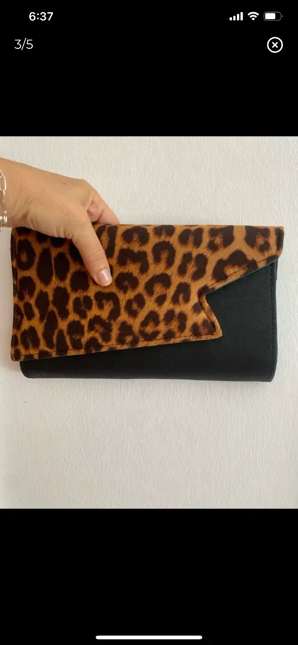 Cartera de mano tipo sobre de la marca Velbet, con solapa de diseño irregular en estampado de leopardo y cuerpo negro. Interior azul claro con bolsillo interno. Ideal para eventos y salidas. 26x16cm
