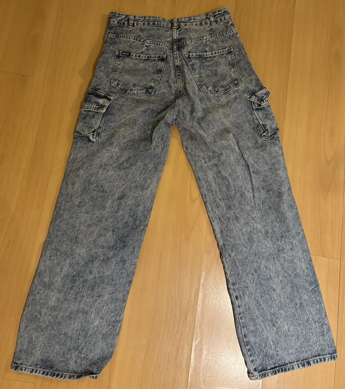 Pantalón cargo de jean azul con múltiples bolsillos, ideal para un look utilitario y moderno. Tiro alto y corte ancho, perfecto para un estilo streetwear.