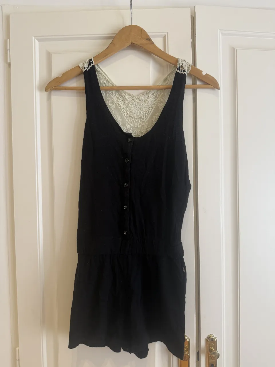 Mono negro con detalles de encaje blanco en el escote y la espalda. Tiene botones en el frente y cintura elastizada. Ideal para un look canchero y femenino. Talle 1/38. Marca 47street