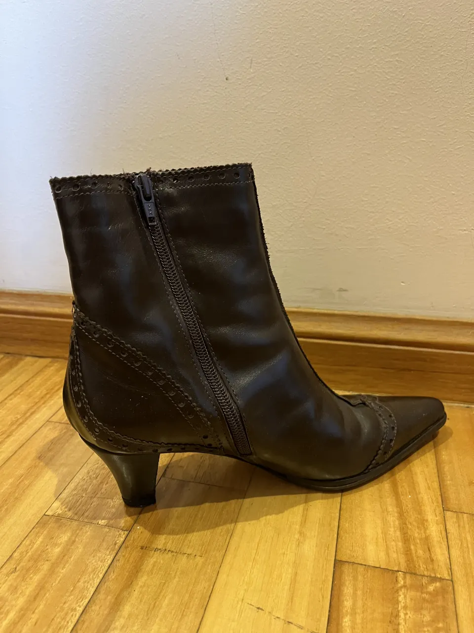 Botitas de cuero marrones con taco y punta fina. Tienen detalles de costuras y perforaciones. Cierre lateral.