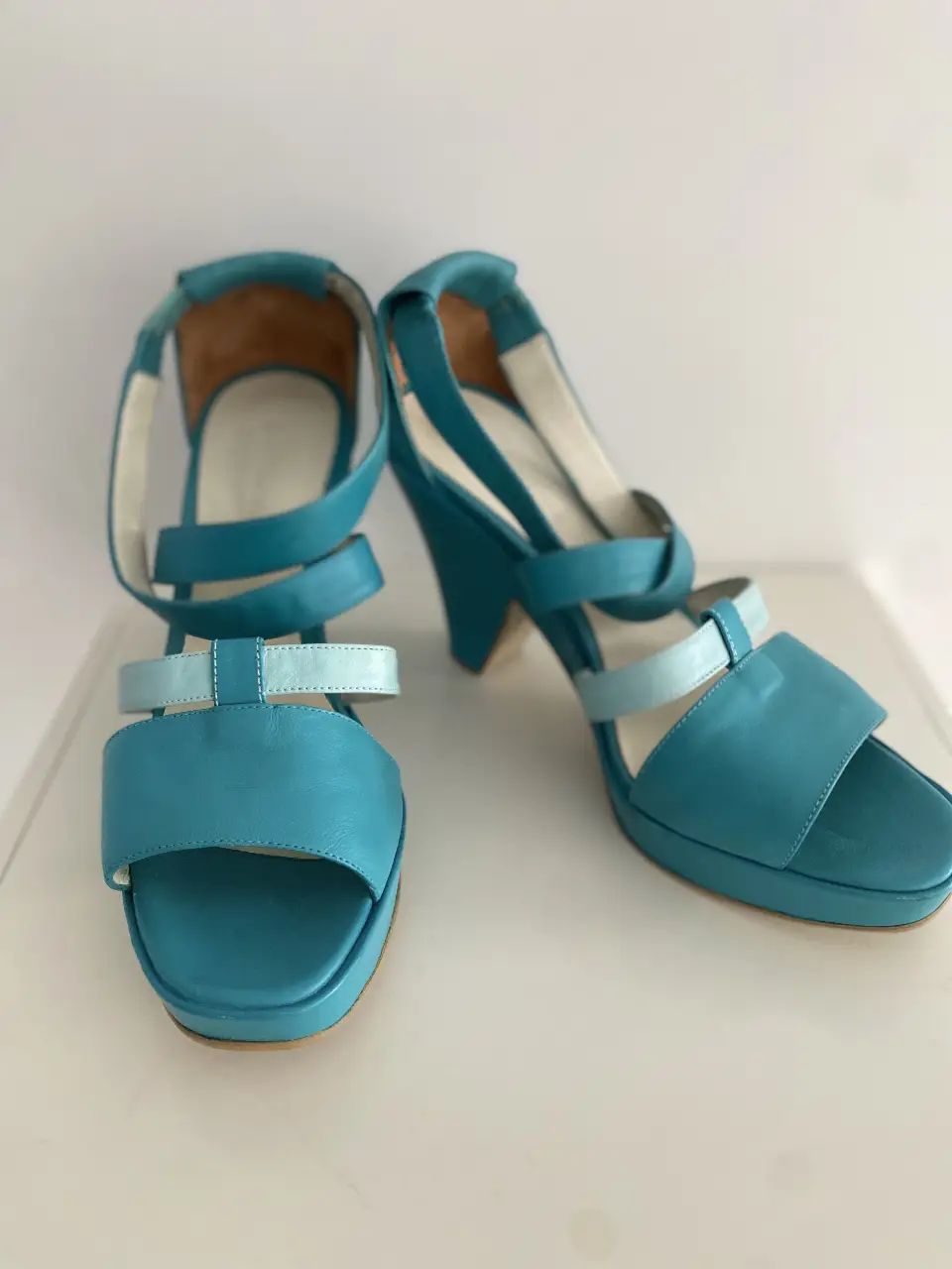 Sandalias de cuero turquesa con detalles en otro tono turquesa más claro. Diseño elegante y moderno, ideales para complementar cualquier look de verano.
