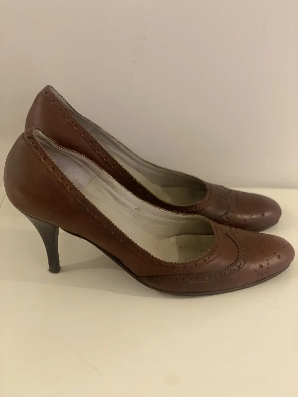 Elegantes zapatos de taco alto color marrón, con detalles de diseño tipo brogue. Ideales para un look sofisticado y femenino.