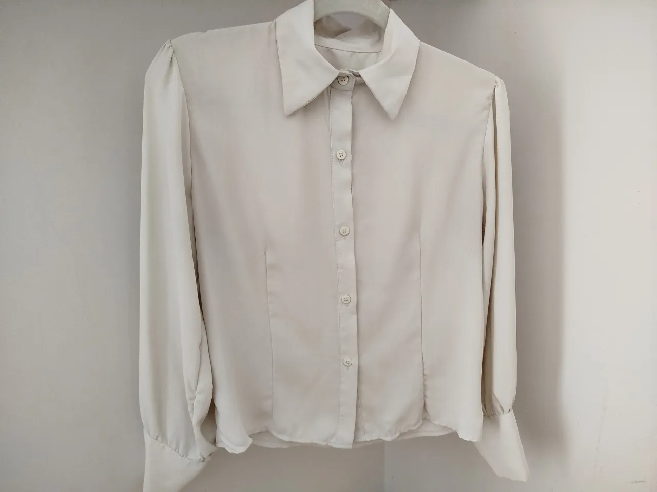 Blusa de mujer en color blanco roto, con mangas largas abullonadas y cuello camisero. Ideal para un look elegante y sofisticado.